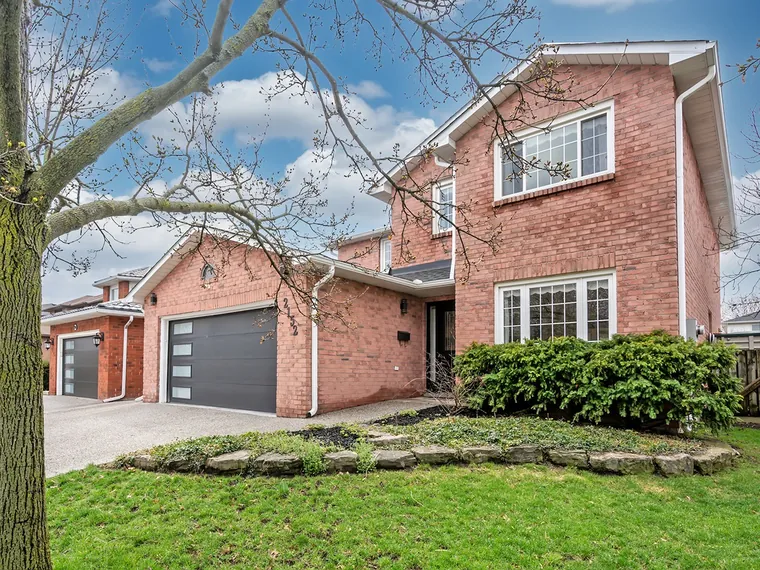 Two-storey red brick detached home with a double garage, white trim and a stone-edged front garden at 2152 Heidi Ave, Burlington, ON